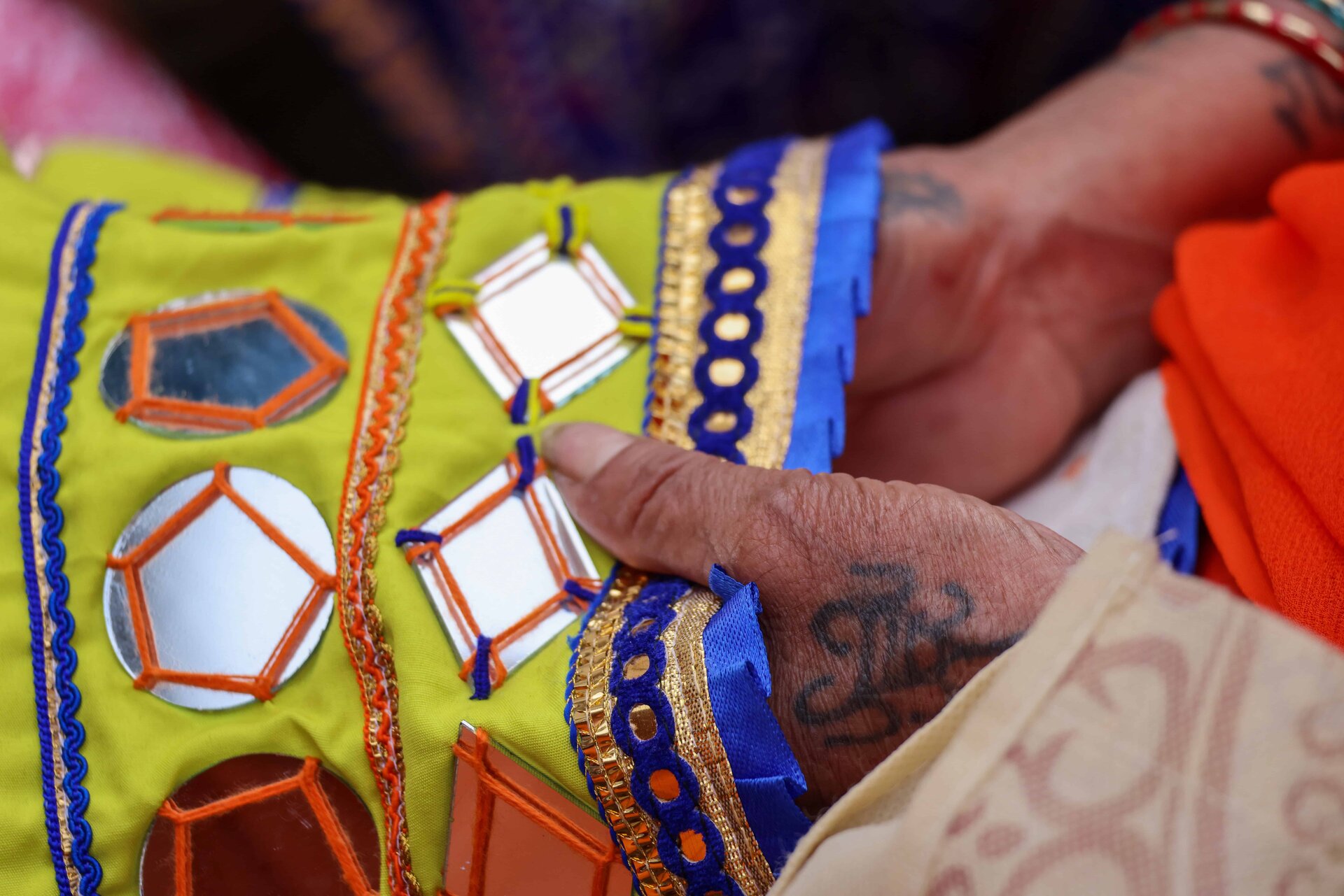 A close-up of a hand gently touching a vibrant textile featuring colorful embroidery and reflective mirrors.