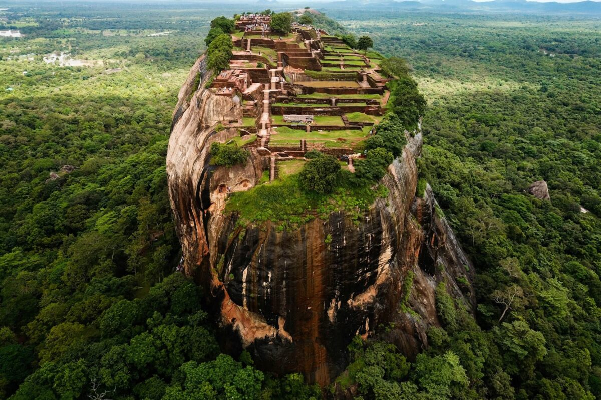 Aerial view of an ancient fortress on a rock formation surrounded by lush green forests.